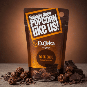 MyEureka Dark Choc Gourmet Popcorn bag with chocolate pieces and popcorn scattered around, warm background.