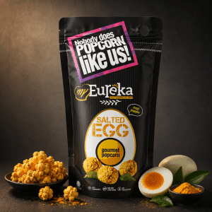 Gourmet salted egg popcorn bag from My Eureka on a dark background, with popcorn clusters and a halved egg for styling.