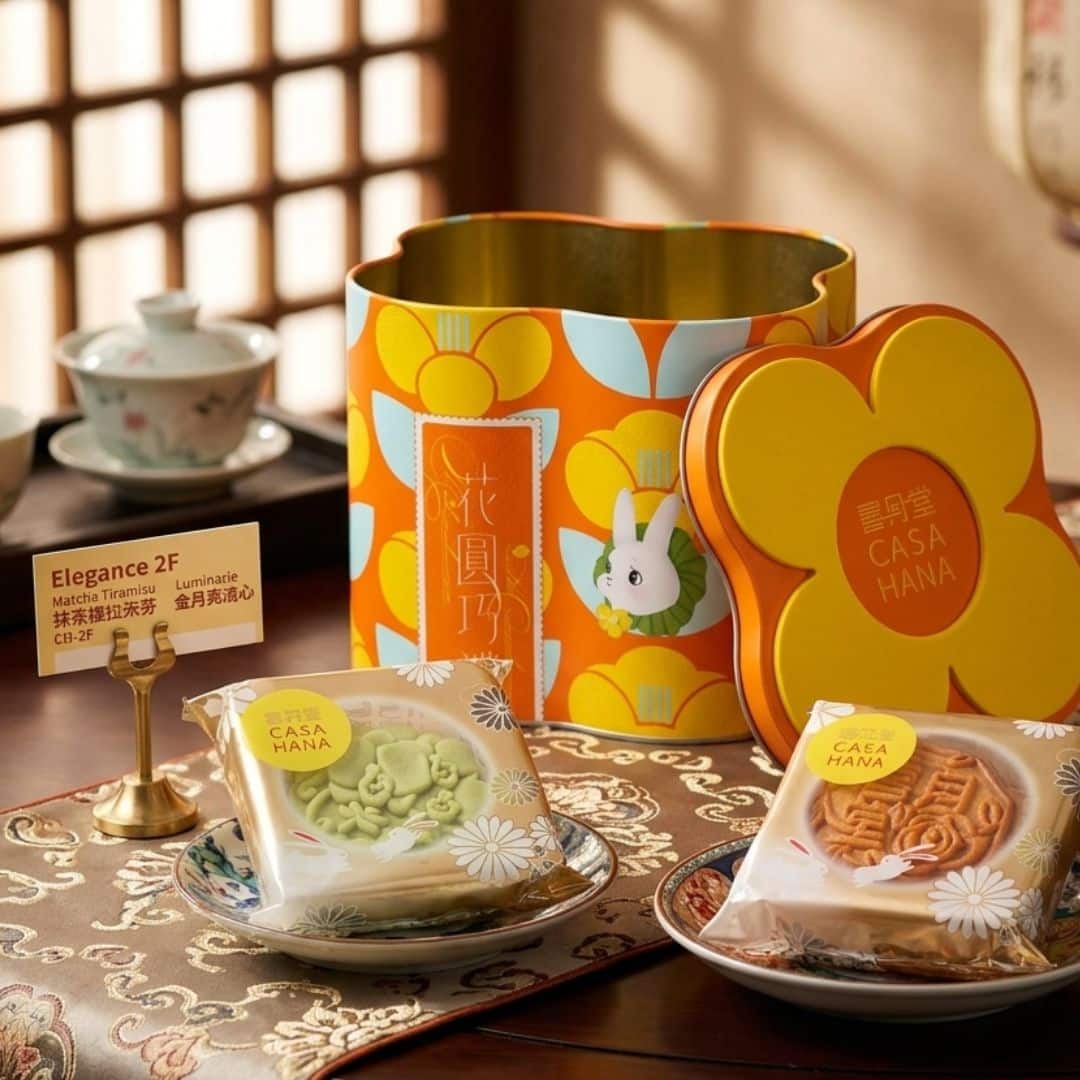 Casahana Mooncake Box Matcha Tiramisu and Luminare 1 | Snack Affair Archives Bright orange floral tin with a yellow lid and bunny motif, surrounded by wrapped Casa Hana cookies on a patterned tablecloth.