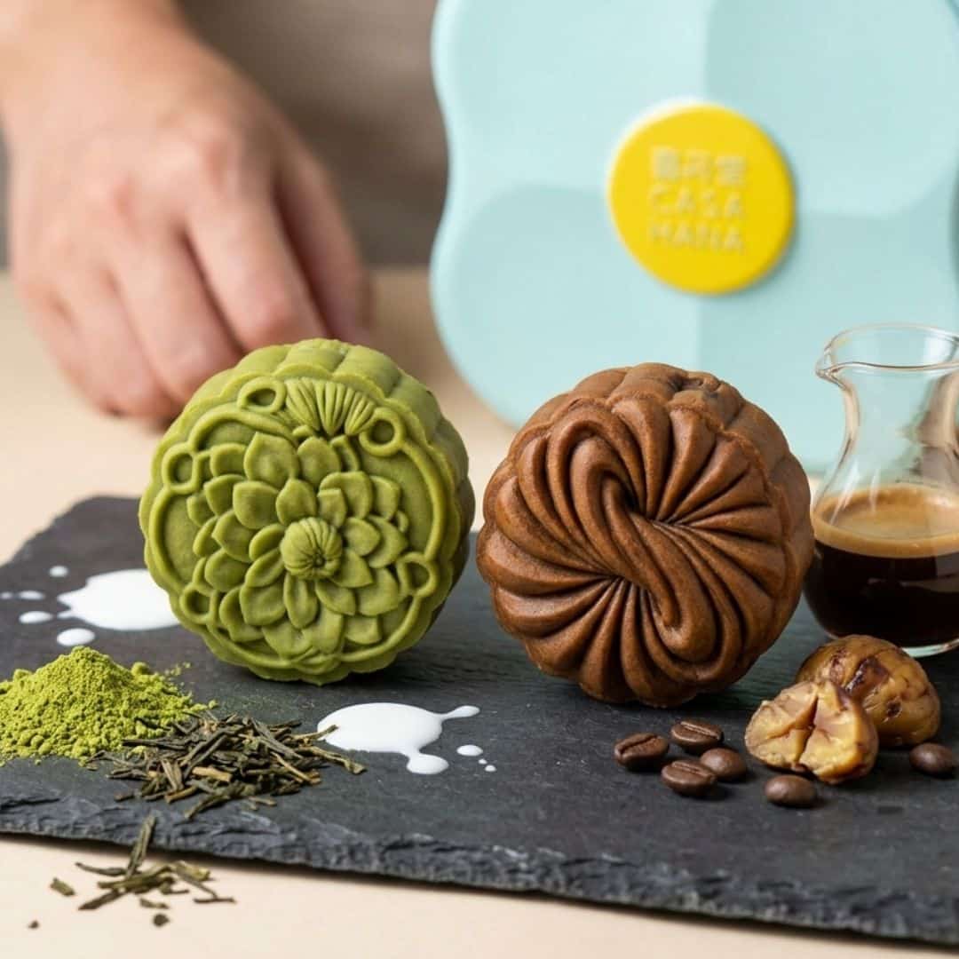Casahana Mooncake Green Tea Espresso | Snack Affair Archives Two ornate pastries on a slate board: a green floral-patterned pastry and a brown swirled pastry, with coffee and spices nearby.