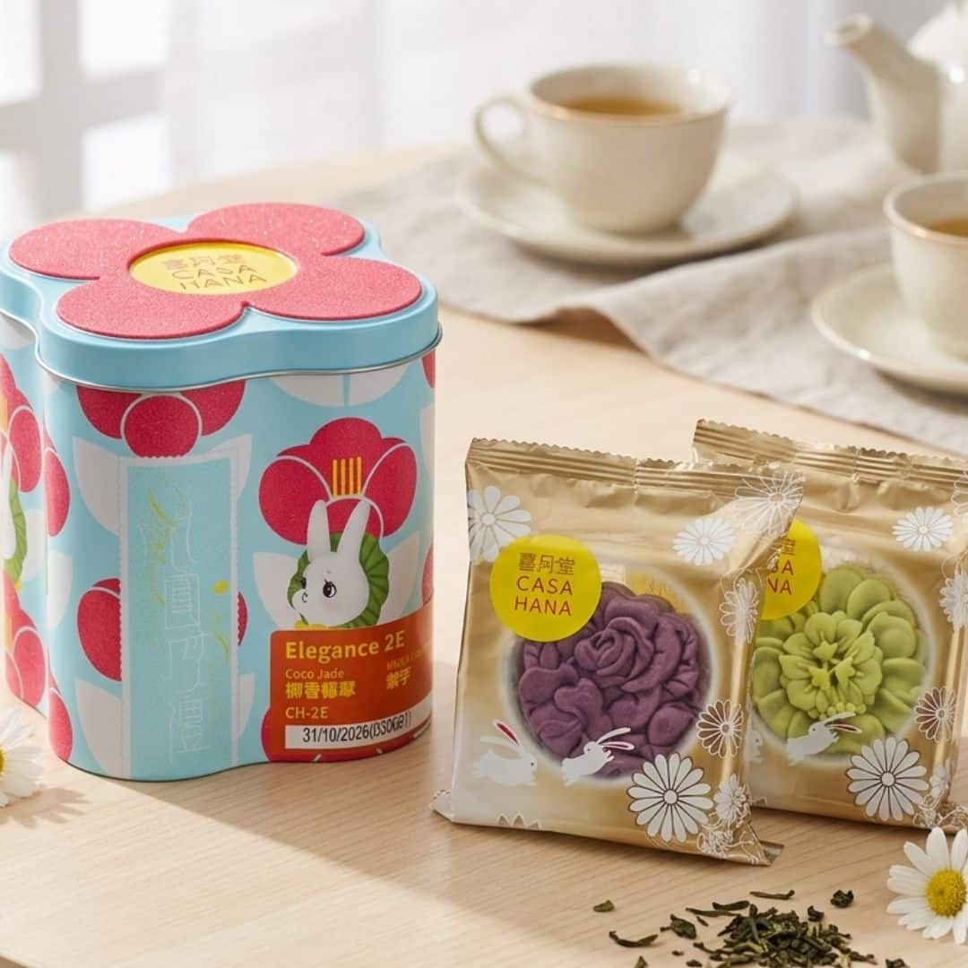 Casahana Mooncake Gift Set Coco Jade Violet Harmony 5 | Snack Affair Archives Pastel blue flower-shaped tin with a rabbit illustration, beside two gold-wrapped cookie packets on a wooden table with tea cups in the background.
