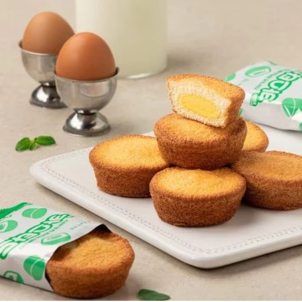 lotte korea custard 12 pcs 2 | Snack Affair Archives Stack of golden-brown round pastries on a white plate, one cut open to reveal yellow custard filling, with eggs in cups in the background.