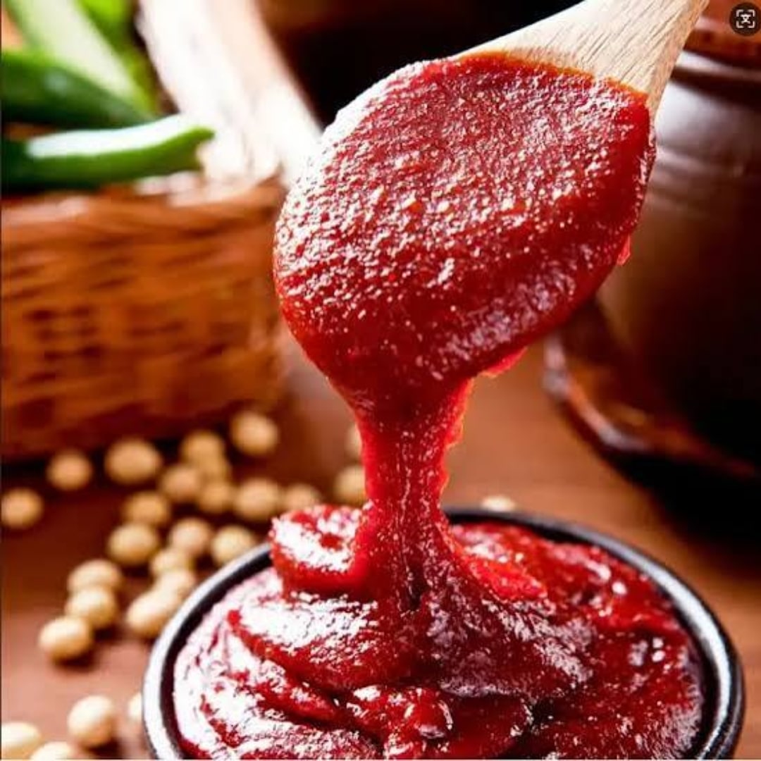 Sajo Gochujang 2 | Snack Affair Archives Close-up of thick red sauce being poured from a wooden spatula into a jar, a glossy, textured drizzle filling the rim.