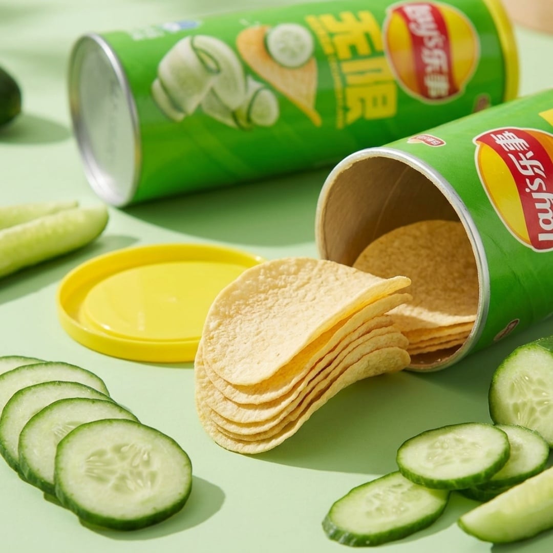 lays cucumber potato chips 1 | Snack Affair Archives Open green can of potato chips with chips spilling out onto a green surface, surrounded by cucumber slices.