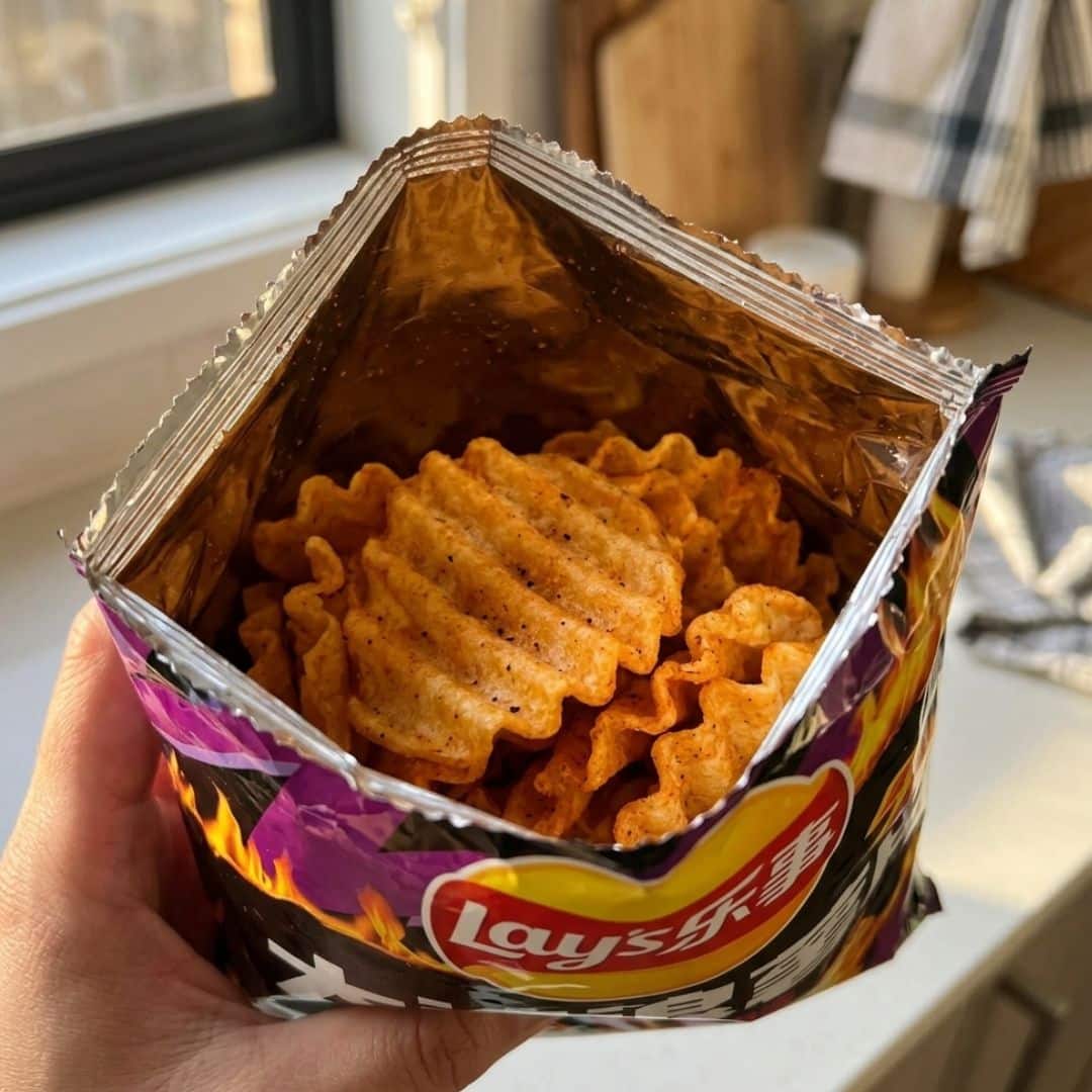 Lays Chips Buldak Spicy Chicken Flavour inside | Snack Affair Archives Open Lay's potato chips bag held near camera, showing ridged, baked chips inside.