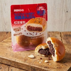 Archives Anpan bun torn open showing sweet red bean filling on a wooden surface with a red snack package in the background.
