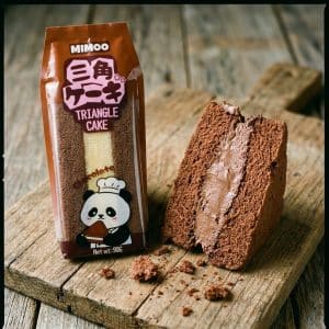 Archives Package of MIMOO Triangle Cake with a panda chef on the wrapper, next to a sliced chocolate triangle cake on a wooden surface.