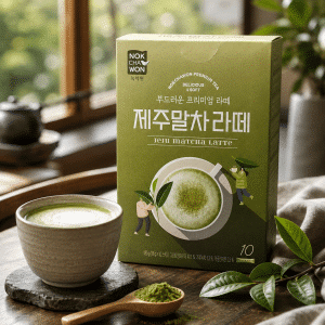 Jukcha Won Jeju Matcha Latte box on a wooden table with a cup of matcha latte and a scoop of matcha powder nearby, leaves in frame