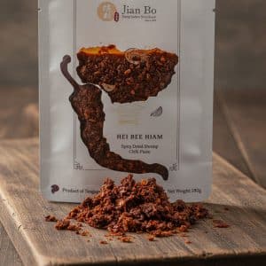 Packaging of Hei Bee Hiam spicy dried shrimp chili paste with paste heap on a wooden surface in front of the bag