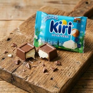 Pieces of milk chocolate with creamy white filling broken on a rustic wooden board, with a blue Kiri chocolate package in the background.