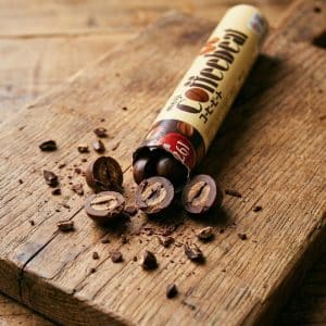 Archives Chocolate-filled candy pieces spill from a beige wrapper onto a rustic wooden board, cross-sections revealing nut centers inside each piece.