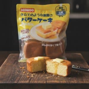 Two halves of a butter sponge cake with melted butter on top, sliced on a wooden board with a yellow MIMOO cake mix bag in the background.