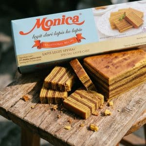 Box of Monica Lapis Legit Traditional Recipe cake with sliced layered cake pieces on a wooden surface